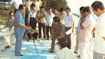 林苍祐在实地视察发展计划时,在海边沙滩上就地摊开地图向官员们作出指示。