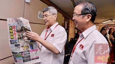 马袖强(左)阅读《光华日报》,观看之前民政党元老会议的报道。旁为刘华才。