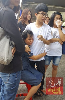 遗孀看着丈夫灵柩伤心欲绝,抱着二儿子耀锋哭成泪人,亲友在旁安慰。