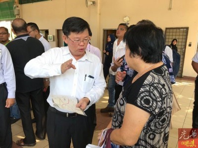 曹观友(左)耐心向不了解免费接驳巴士服务路线图的民众讲解。