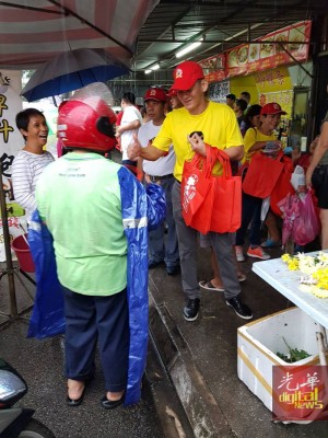 王耶宗冒着雨到大路后巴刹走访拜票,并分派环保袋给民众。