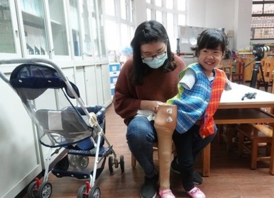 幼儿园老师协助又立穿上义肢。