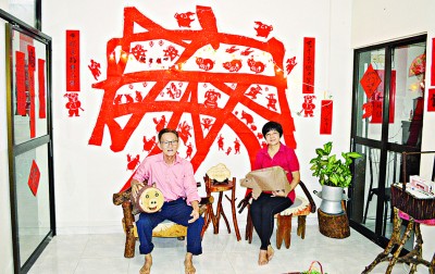 郭春安与李秋云在贴着多只猪围绕着“家”字的客厅，恭祝大家猪年新年快乐。