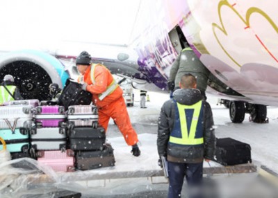 工作人员冒风雪搬运旅客行李。