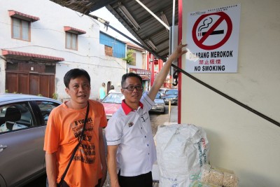 刘志良（右）赠送禁烟告示牌给老街其中一名商家蔡国财，并直接张贴在商店显眼处。