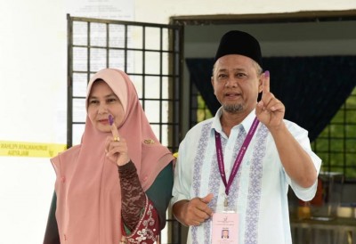 国阵候选人查卡利亚与妻子一早完成投票后，展示墨染的手指。