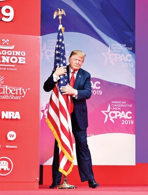 特朗普步入讲台致词时显得非常兴奋，一脸陶醉地拥抱一面美国国旗。（法新社照片）
